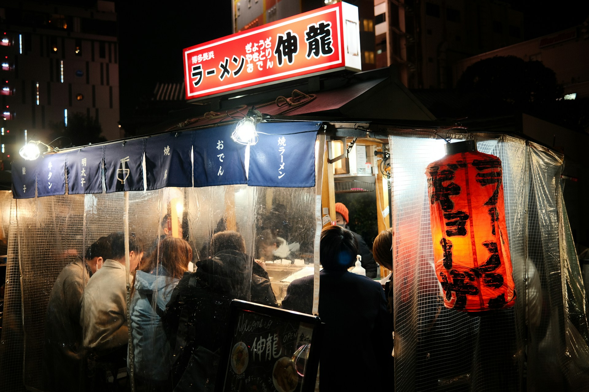 Patrons crowd a glowing ramen yatai stall on a nighttime street in Fukuoka, Japan